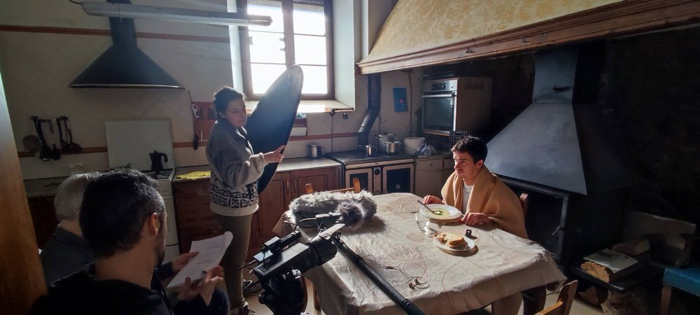 El equipo graba a una mujer sentada a la mesa de una cocina antigua, con pértiga de sonido y cámara.
