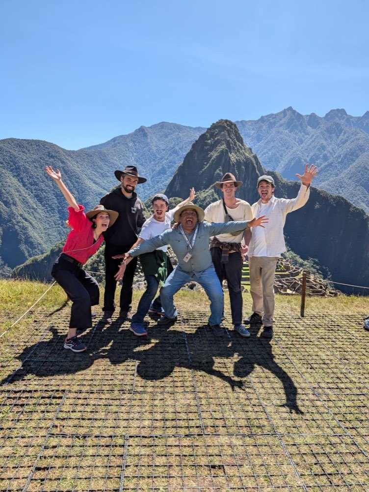 Seis personas del equipo posan con los brazos en alto ante las montañas de Machu Picchu.
